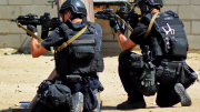 Two tactical officers in full ballistic gear kneeling behind cover during a training exercise, showcasing modern body armor and protective equipment.
